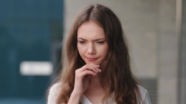 Portrait young caucasian millennial girl pensive puzzled woman female model creative student standing outdoors city thinking planning pondering deeply in thoughts comes up with idea happy smiling — Stock Video