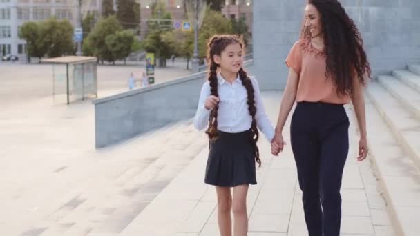 Szülő anya anya kisgyerekkel lány iskoláslány gyermek sétál az utcán a városban összebújva beszélő beszélgetés mosolyogva. A spanyol anyuka elvezeti a lányát az iskolába, együtt mennek órára, beszélgetünk. — Stock videók