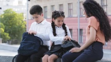İspanyol anne ile ilgilenen anne anne anne kadın öğle yemeği için çocuklara yemek veriyor sandviç yiyor sırt çantasındaki öğrencilere, öğrencilere, kızlarına ve oğluna okuldan önce dışarıda oturmalarına yardım ediyor.