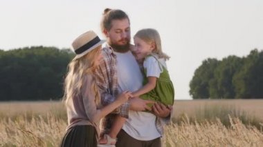 Mutlu beyaz aile çiftçileri küçük kızlarıyla birlikte genç ebeveynler yaz tatilinde dışarıda buğday tarlasında durup gülerek doğayla iç içe konuşarak eğleniyorlar.
