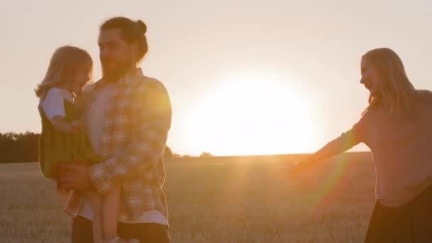 Silhouettes three people happy caucasian family active cheerful parents with little daughter kid girl playing game airplane flight pretend flying standing in wheat field outdoors having fun enjoy play — Stock Video