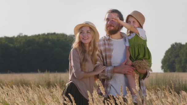 Glad kaukasisk familj kärleksfulla föräldrar med liten dotter barn stående i vetefält i naturen sommardag, far håller liten flicka visar med finger riktning prata, semestrar utomhus — Stockvideo