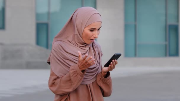 Porträtt av glada muslimska affärskvinna njuta av framgång på mobiltelefon utomhus. Närbild glad islamisk flicka läser goda nyheter på mobiltelefon på gatan. Överraskad etnisk dam i hijab firar segern — Stockvideo