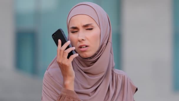Moslim jonge vrouw islamitisch meisje dragen hijab spreekt praten door mobiele telefoon antwoorden oproep bezorgd problemen met slecht signaal cellulaire communicatie netwerkverlies lage batterij moeilijk te horen gehoorproblemen — Stockvideo