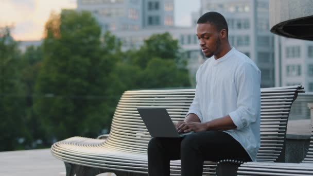 Afro américain gars créatif homme d'affaires africain travailleur indépendant étudiant entrepreneur travaillant à distance avec ordinateur portable assis à l'extérieur en tapant email chat en ligne, application e-learning avec ordinateur en ville — Video