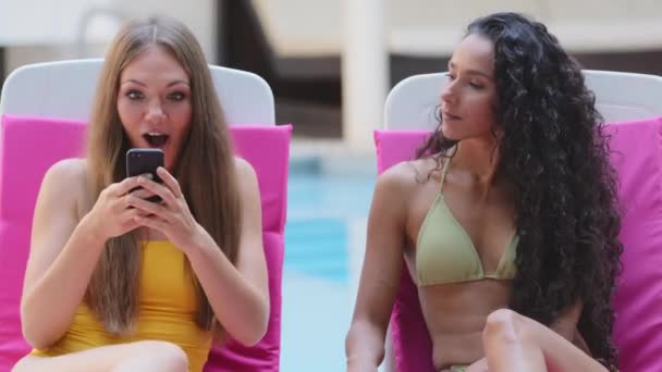 OMG reaction. Millennial ecstatic girl received amazing news virtual message from boyfriend, winning lottery yells joyfully feels euphoric. Cheerful happy European Spanish girlfriends in bathing suits — Stock Video