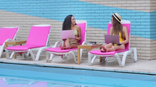 Sorrindo jovens multirraciais mulheres caucasianas amigos hispânicos relaxando na beira da piscina, navegando conteúdo meadia social on-line e compartilhar usando laptop, enquanto desfruta de lazer perto da piscina em férias de verão — Vídeo de Stock