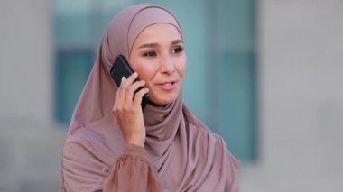 Arap genç, mutlu, başörtülü kadın şehirde cep telefonuyla konuşuyor. Başörtüsü takan şık Müslüman kız cep telefonundan konuşuyor, sohbet ediyor.