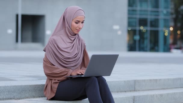 Gyönyörű muszlim lány hidzsáb sál iszlám nő vezeték nélküli laptop dolgozik a szabadban nézi kamera pozitívan mosolyog. Sikeres arab szabadúszó egyetemi hallgató, aki a városban tanul — Stock videók