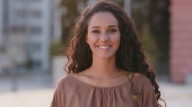 İspanyol genç, güzel, mutlu, mutlu, kaygısız, hevesli, esmer kız model sağlıklı beyaz dişli, kameradan memnun, şehirde gülümseyen müşteri dişçisine gülümseyen bir kız.