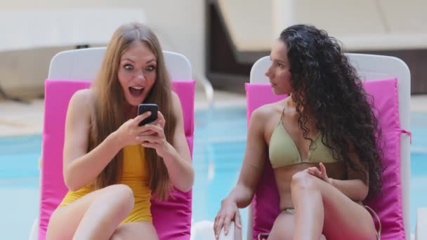 Heyecanlı, çoklu etnik kökenli, Latin kökenli genç kızlar tatillerde havuz başında akıllı telefon kullanarak mutluluktan uçuyorlar. Mutlu kız arkadaşlar harika bir ekommersi satışı teklifi alıyorlar, başarıyı kutluyorlar. — Stok video