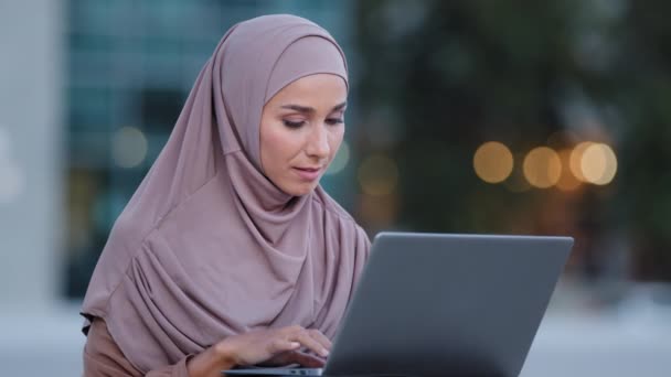 Ritratto di musulmana giovane donna utente donna d'affari studentessa islamica in hijab si siede sulla strada guardando nel computer portatile si sente sorpresa legge buone notizie online in Internet funziona da remoto riceve offerta e-mail — Video Stock