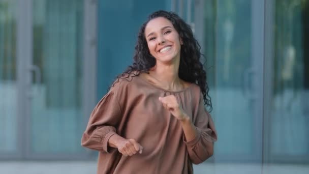 Enthusiastic happy hispanic woman young active carefree young adult girl brunette beautiful attractive lady looking at camera celebrating dancing moving hands victory dance having fun outdoors in city — Stock Video