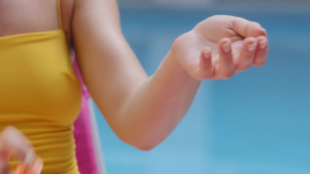 Primer plano joven turista mujer blanca que descansa tomando el sol cerca de la piscina del hotel aplicando agente bronceador. Manos femeninas sosteniendo la botella de loción bloqueador solar, crema hidratante protector solar. Chica europea, Cosméticos para el cuidado — Vídeos de Stock