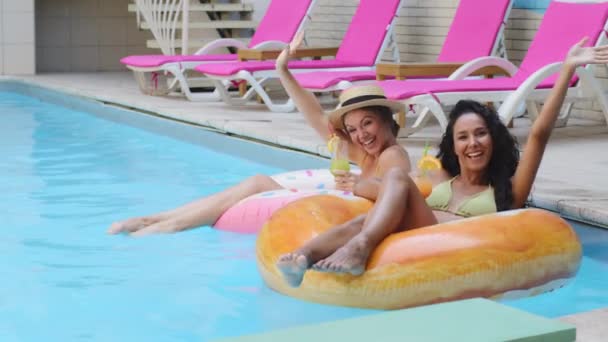 Alegre bronceado tomar el sol novias celebración cócteles disfrutando de verano en la piscina le invitan. Multiracial mujeres estudiantes europeo rubia chica y hispano joven agitando las manos hola ven aquí unirse — Vídeo de stock