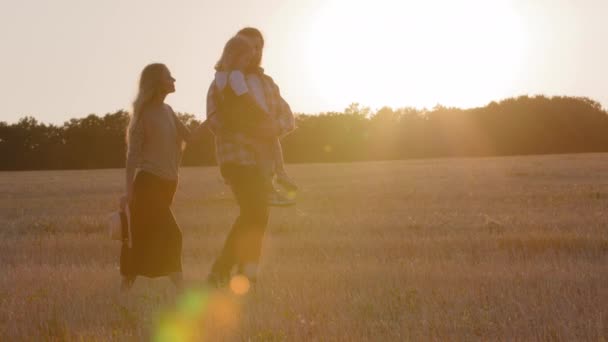 Διακοπές Σαββατοκύριακο σε εξωτερικούς χώρους στη φύση τρεις σιλουέτες αγρότες στο φόντο του ηλιοβασιλέματος ακτίνες του ήλιου οικογένεια με παιδί παιδί περπάτημα στο χωράφι με σιτάρι θα περπατήσει στο φως του ήλιου το καλοκαίρι το βράδυ — Αρχείο Βίντεο