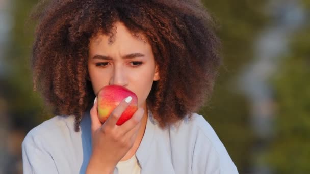 Close up Afro-americano mulher africana encaracolado menina sentado ao ar livre farejadores vermelho fresco maduro maçã deliciosa fruta sentimento frustrado perda de sintoma olfato coronavírus doença vívido vírus olhando para a câmera — Vídeo de Stock