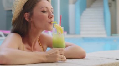 Mayolu, şapkalı, spa otelinde yaz havuzunda dinlenen ve samanla buz kokteyli içen sevimli Avrupalı genç bir kız. Çekici bin yıllık kadın turist bir bardak içkiyle keyifli bir tatil yapıyor.