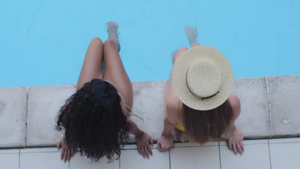 Closeup top view γυναίκες τουριστικές φίλες χαλάρωση ηλιοθεραπεία κατά τη διάρκεια των καλοκαιρινών διακοπών σε πολυτελές ξενοδοχείο spa. Νεαρές μαυρισμένες, λεπτές γυναίκες κουνάνε τα πόδια τους κάνοντας κύμα στην μπλε πισίνα. — Αρχείο Βίντεο