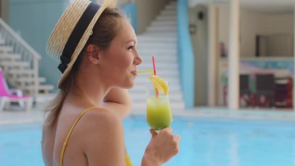 Feliz despreocupado milenario europeo chica de piel clara en traje de baño y sombrero relajante en la piscina con un vaso de bebida refrescante. Atractiva joven turista disfrutando de vacaciones bebiendo cóctel de hielo — Vídeos de Stock