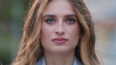 Aşırı yakın plan kadın ciddi yüzü, doğal makyaj mavisi gözleri açık havada poz veren kameraya bakıyor. Bin yıllık genç beyaz iş kadını model sarışın kız bakışları. Dışarıda 30 'lu yaşlarda bir kadın resmi var.