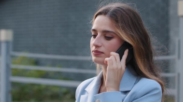 Egy közeli fiatal üzletasszony beszél mobilon a város utcájában. Kaukázusi 30-as évekbeli lány veszi fel a telefont a szabadban. Millenniumi ügyfél hölgy nő komoly diák hívás okostelefon kívül — Stock videók