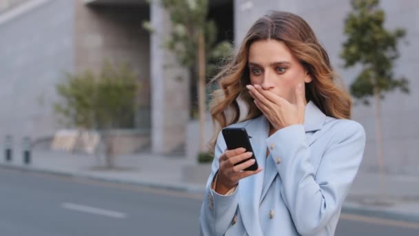 Kavkazské obchodní žena venku držet mobilní telefon číst nepříjemné sms hrozné zprávy pocit rozhořčení zakrývá ústa šokovaný obličej. Špatné upozornění z bankovního zablokovaného účtu zlomený úžas smartphone — Stock video
