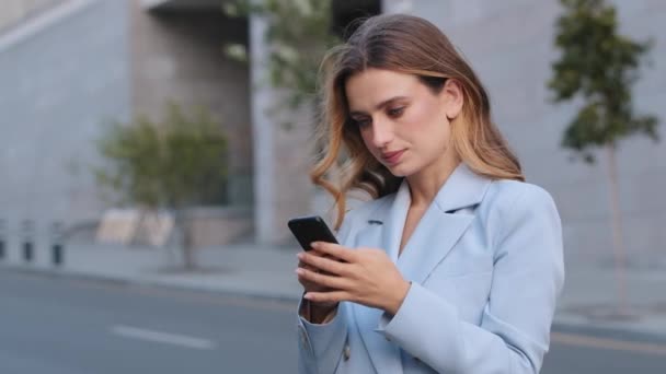 Ernsthafte kaukasische junge elegante Geschäftsfrau, die Social-Media-Anwendung auf dem Smartphone nutzt, erhält Nachrichten, die mit dem Handy im Freien getippt werden. — Stockvideo