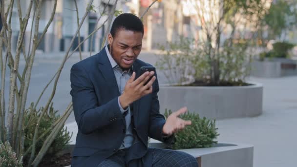 Irate infastidito arrabbiato afroamericano nero uomo d'affari in possesso di smartphone guardando lo schermo del telefono cellulare fare videoconferenza di lavoro insoddisfatto del risultato della negoziazione, cambiamento, termini proposti — Video Stock