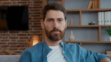 Evdeki beyaz adamın portresi ciddi bir şekilde kameraya bakıyor. Evin içinde, rahat bir oturma odasında orta yaşlı, sakallı, kendine güvenen, kendine güvenen bir erkek. Kanepede dinlenen ev sahibi.