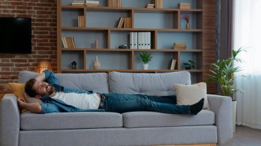 Kafkasyalı yorgun bir adam evdeki oturma odasında rahat bir kanepeye uzanıp dinleniyor. Orta yaşlı bir ev sahibinin evinde dinleniyor. Haftasonu evde dinleniyor.