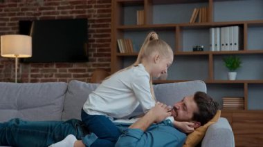 Evde mutlu beyaz bir aile kızıyla gıdıklayan babayı oynuyor. Gıdıklayan bir baba kanepeye uzanıyor. Sevgi dolu küçük bir çocukla oynuyor.