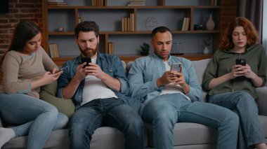 Odaklanmış dört farklı arkadaş cep telefonlarını aşırı kullanıyor internet sosyal medya bağımlılığı evde sıkıcı partiler akıllı telefonlara bakıyor çok ırklı erkekler birbirini görmezden geliyor