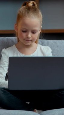 Kafkasyalı küçük kız evdeki kanepede dizüstü bilgisayar kullanıyor. Çocuk kızı, oturma odasında bilgisayar kullanıyor. Modern teknoloji ve genç nesil liseli kız online sanal oyunlar oynuyor.