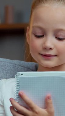 Kafkasyalı gülümseyen mutlu küçük kız, evde ders kitabı yazıyor uzaktan eğitim öğreniyor, ilkokulda ilkokuldan zevk alan kız öğrencileri okuyor, oturma odasında ödevlerini yazıyor.