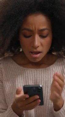 Üzgün üzgün afro-amerikan kadın kötü haber okuyor evde cep telefonlu kadın hayal kırıklığına uğradı kız haber vermeyi reddetti akıllı telefon sorunu uygulaması
