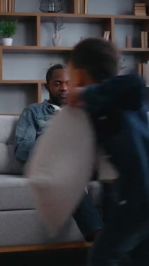 Afro-Amerikan aile babası online çalışıyor yastık oynayan yaramaz çocuklar dizüstü bilgisayarla babalarıyla kavga ediyorlar cep telefonlarıyla konuşuyorlar evde gürültülü işler yapıyorlar iki çocuk çocukları rahatsız ediyor etrafta geziniyorlar