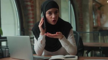 Sinirli, tesettürlü Müslüman iş kadını cep telefonu tartışması yapıyor. İslamcı iş kadını, akıllı telefon sorunu olan ve dizüstü bilgisayarla uğraşan kadın sorununu vurguladı.