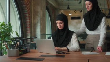 Müslüman İslami intörn yeni işçi işkadını tesettür sorunu dizüstü bilgisayarla zor bayan ofis liderinden yardım istemek çevrimiçi hizmet veren iki iş kadını takımı