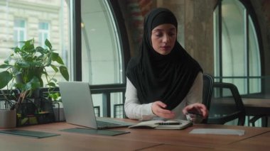 Ofiste dizüstü bilgisayarda yazı yazan Müslüman bir iş kadını, akıllı telefon uyarısıyla hayal kırıklığına uğramış, endişeli ve endişeli bir kadın olarak cep telefonuyla SMS mesajı aldı.