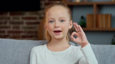 Kafkas mutlu çocuk kız çocuğu portresi. Tamam işareti gösteriyor. Evdeki kameraya bakıyor. Mutlu tasasız kız öğrenci gösterisi.