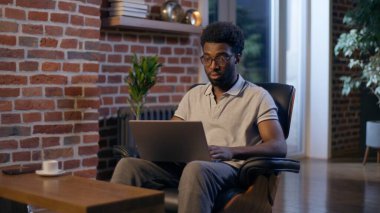 Afrikalı Amerikalı iş adamı iş adamı gece ofisinde dizüstü bilgisayarı yazıyor. İnternette fazla mesai yapıyor. Son teslim tarihi ödevini çalışıyor.