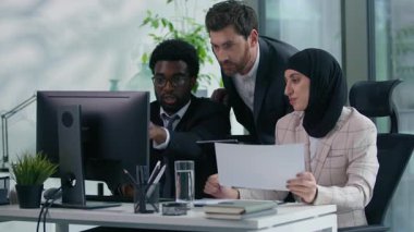 Ofisteki çok kültürlü iş arkadaşları çok ırklı üç iş arkadaşı birlikte çalışıyorlar. Çeşitlilik ortakları bilgisayar ve kağıt üzerinde veri analizi yapıyorlar.