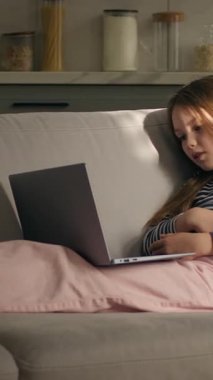 Kafkasyalı küçük çocuk evde dizüstü bilgisayar teknolojisiyle video konuşması yapıyor. Kanepeye uzanmış gülüyor, kız konuşmaları yapıyor. İnternette sanal film izliyorlar.