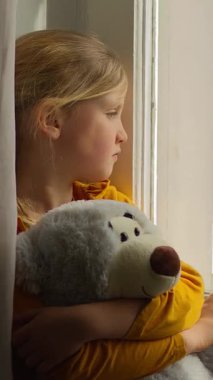 Hüsrana uğramış Kafkas kız çocuk yetim kız elinde oyuncak ayıyla pencereden bakan kız çocuğu sıkılmış kurban masumiyeti. Depresyonda. Evlatlık velayetini bekliyor.