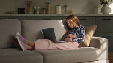 Kafkasyalı küçük çocuk evde dizüstü bilgisayar teknolojisiyle video konuşması yapıyor. Kanepeye uzanmış gülüyor, kız konuşmaları yapıyor. İnternette sanal film izliyorlar.