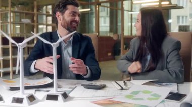 Neşeli Kafkasyalı iş kadını rüzgar türbini modelini tartıştı. Gülüşmeler eko enerji ofisini işaret etti. Sürdürülebilir kalkınma, dayanışma kağıt bürosu.