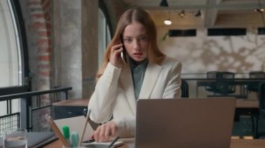 Kafası karışık, çoklu görev sahibi, beyaz kadın iş kadını, dizüstü bilgisayarla notlar yazıyor cep telefonuyla konuşuyor, kötü haber, aşırı çalışan işveren kız konuşuyor.