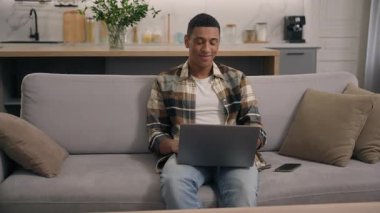 İyi ki gülümseyen Afro-Amerikalı bir adam bilgisayarla video oyunu oynuyor. Ev sahibi olan erkeğin evinde çalışıyor, uzaktan sohbet ediyor, sosyal medya, internet teknolojisi siber-uzay elemanı bilgisayar kullanıyor.