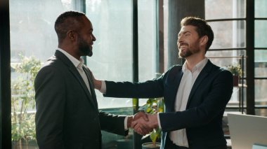 İki etnik çeşitlilikte iş adamı şirket ofisinde tokalaşıyor, konuşuyor, çeşitli beyaz iş adamları el sıkışıyor, gülümseyen Afrikalı Amerikalı erkeğe hoş geldin diyor.